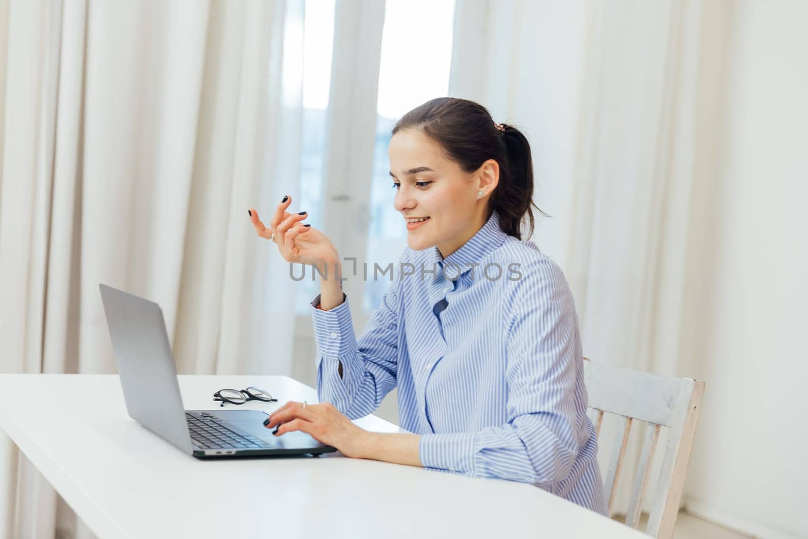 Image of young pleased happy cheerful cute beautiful business woman sit indoors in office using laptop computer listening music with earphones.