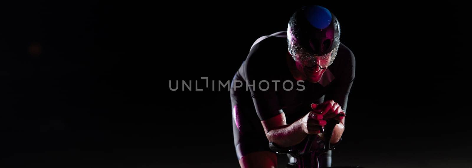 A triathlete rides his bike in the darkness of night, pushing himself to prepare for a marathon. The contrast between the darkness and the light of his bike creates a sense of drama and highlights the athlete's determination and perseverance