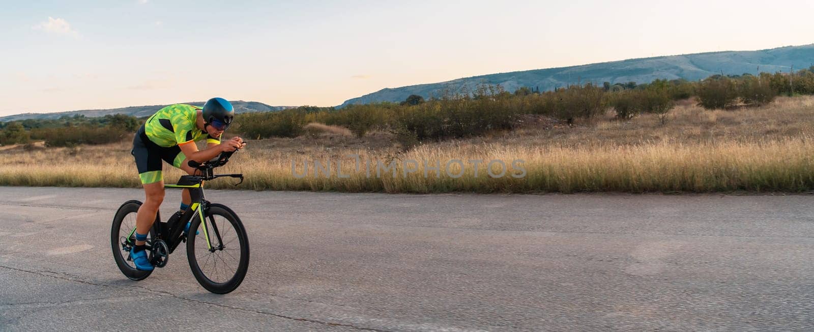 Triathlete riding his bicycle during sunset, preparing for a marathon. The warm colors of the sky provide a beautiful backdrop for his determined and focused effort. by dotshock