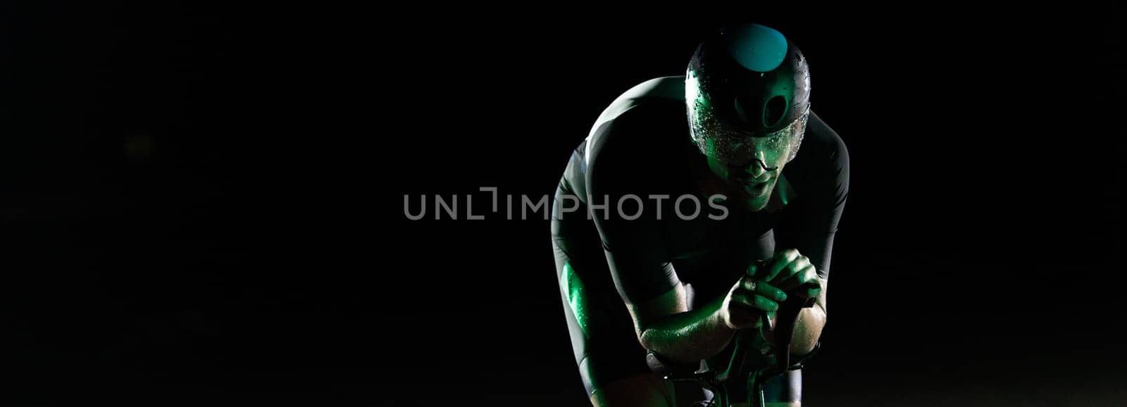 A triathlete rides his bike in the darkness of night, pushing himself to prepare for a marathon. The contrast between the darkness and the light of his bike creates a sense of drama and highlights the athlete's determination and perseverance