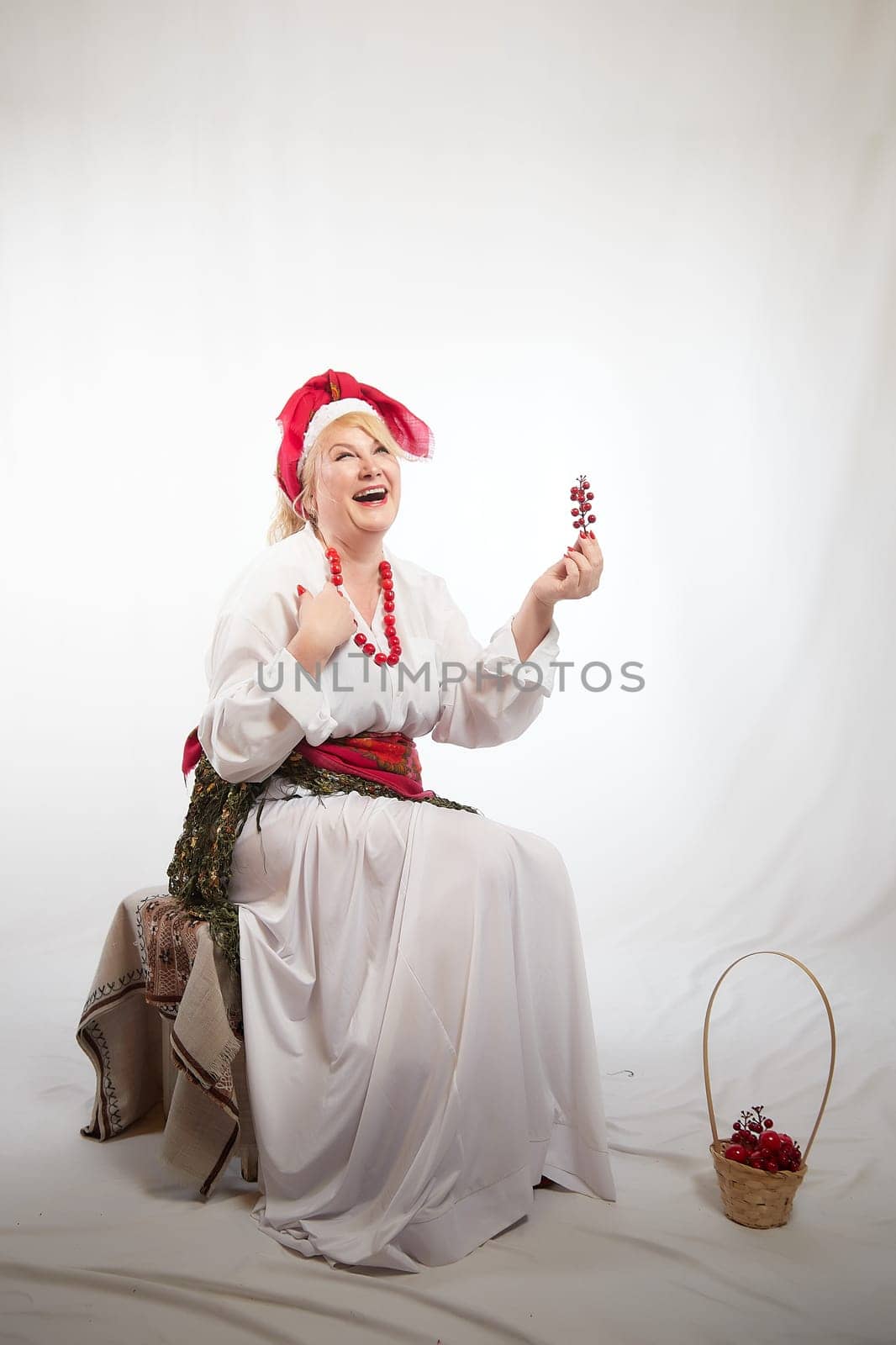 Portrait of heerful funny adult mature woman solokha with red berries. Female model in clothes of national ethnic Slavic style. Stylized Ukrainian, Belarusian or Russian woman in comic photo shoot by keleny
