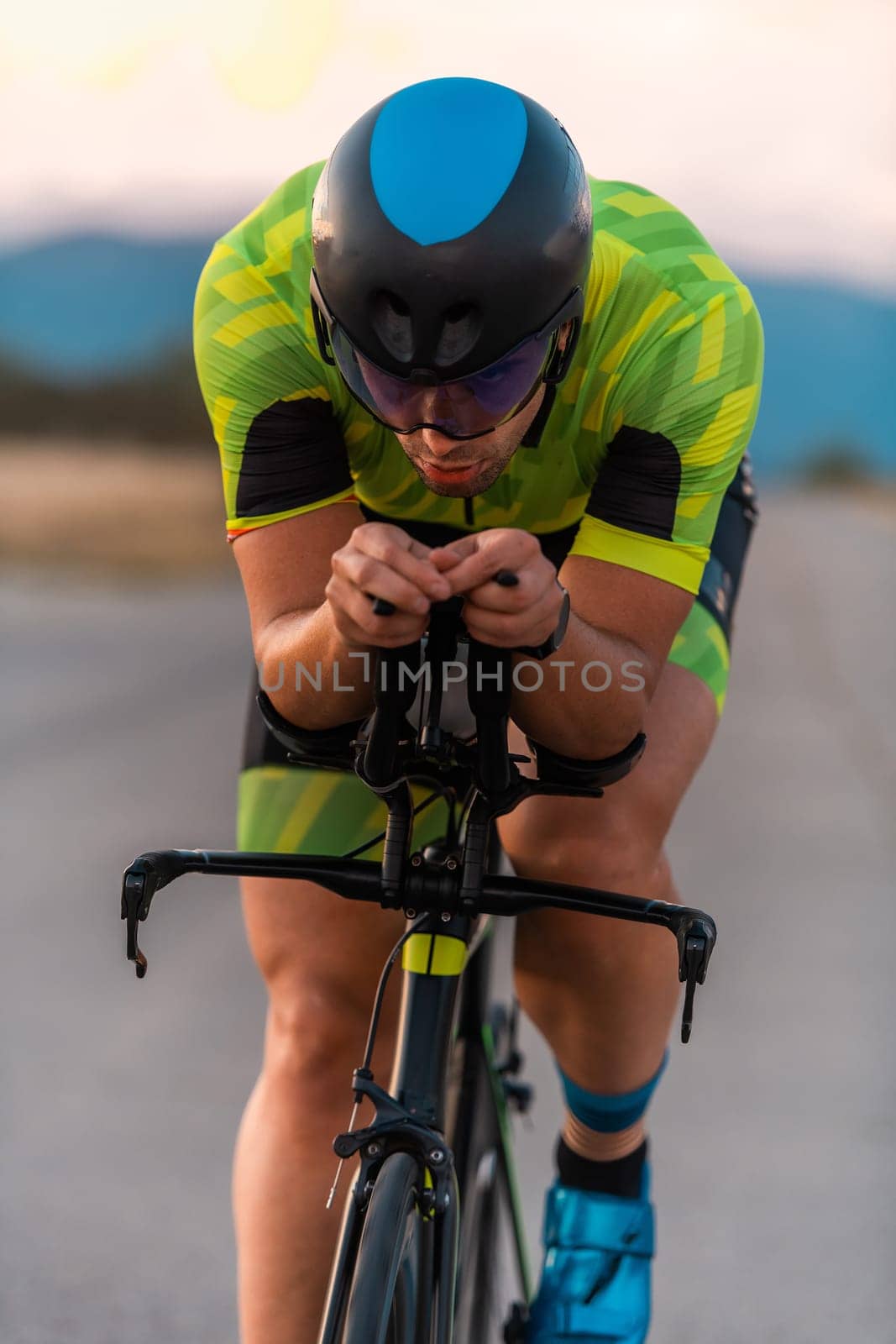 Close up photo of triathlete riding his bicycle during sunset, preparing for a marathon. The warm colors of the sky provide a beautiful backdrop for his determined and focused effort