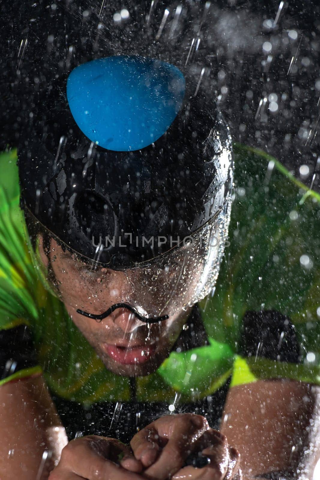 A triathlete braving the rain as he cycles through the night, preparing himself for the upcoming marathon. The blurred raindrops in the foreground and the dark, moody atmosphere in the background add to the sense of determination and grit shown by the athlete