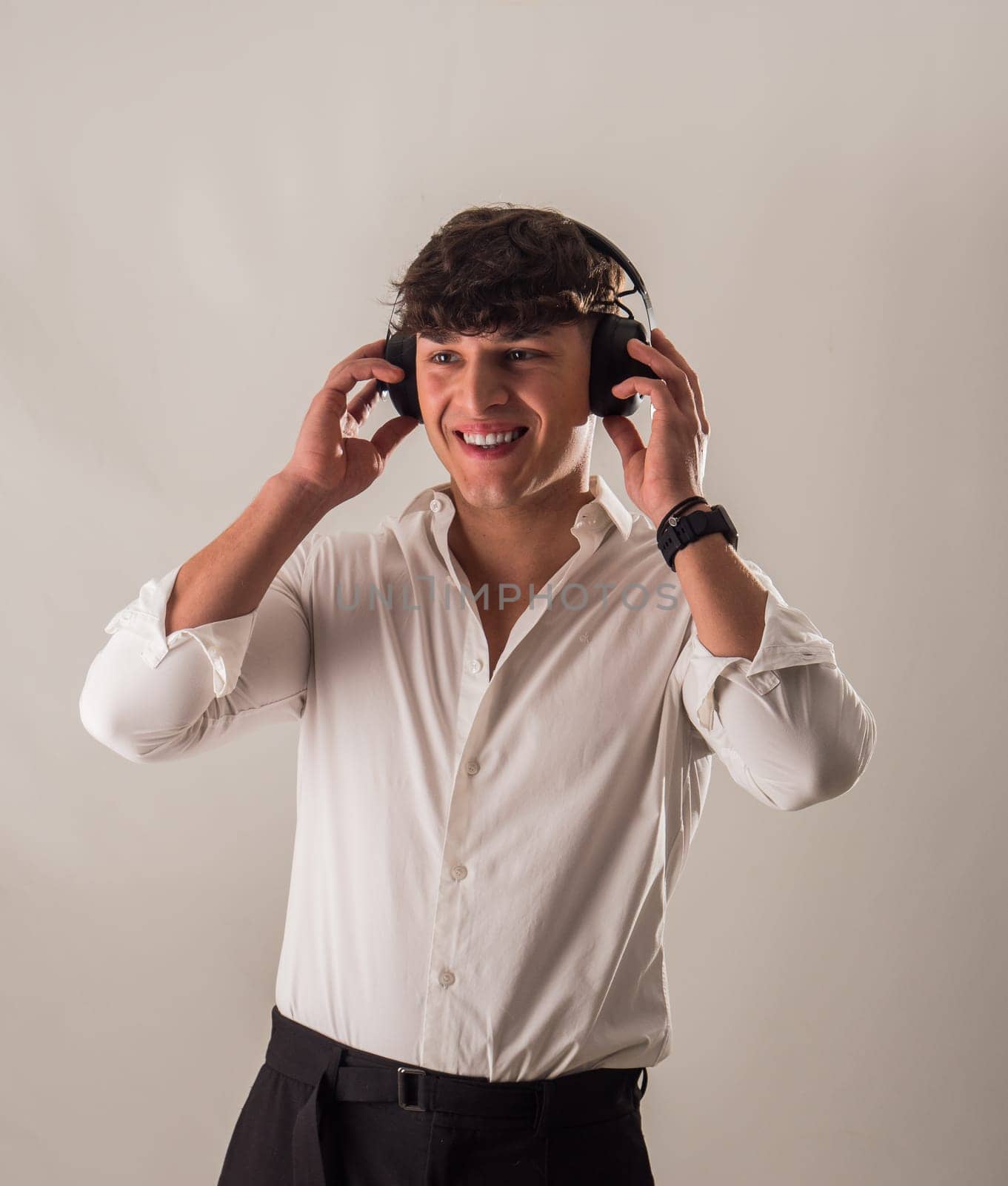 A young handsome man in a white shirt is listening to music on headphones, in studio shot
