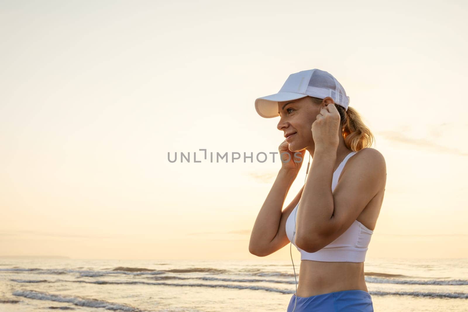 a girl of European appearance in sportswear listens to music on headphones on the seashore during a morning jog. High quality photo