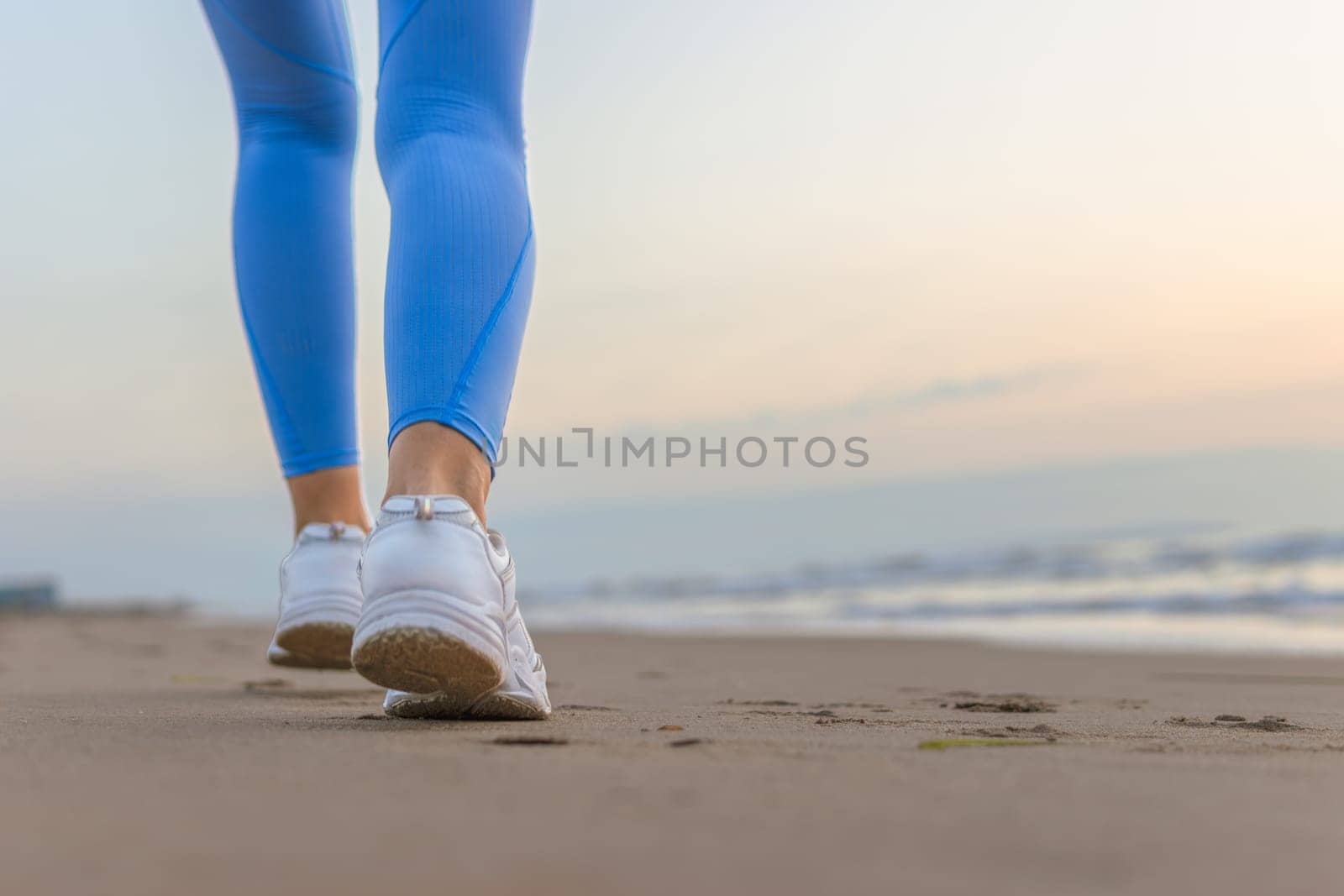 legs of a girl in blue leggings and sneakers running along the beach with space for inscription. High quality photo