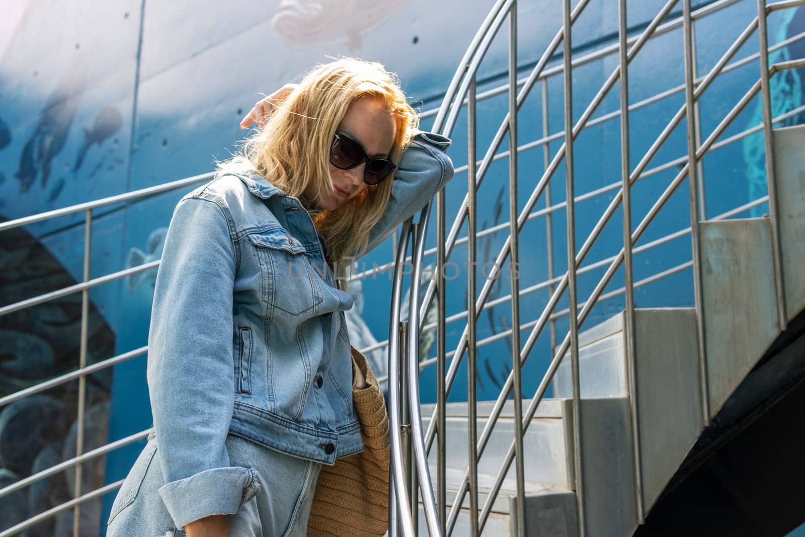 Portrait of young woman wearing a denim jacket with backpack posing on background by PopOff