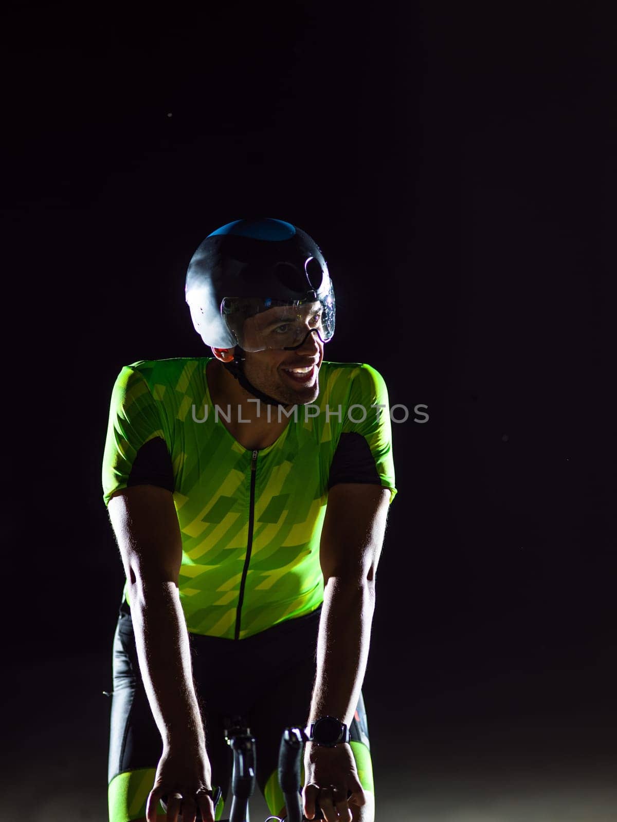 A triathlete rides his bike in the darkness of night, pushing himself to prepare for a marathon. The contrast between the darkness and the light of his bike creates a sense of drama and highlights the athlete's determination and perseverance