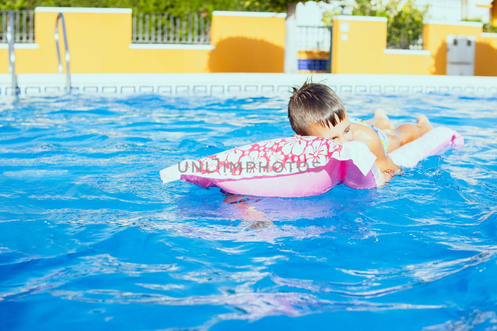 Happy boy resting on a pink inflatable mattress in the pool, there is a place for an inscription. High quality photo