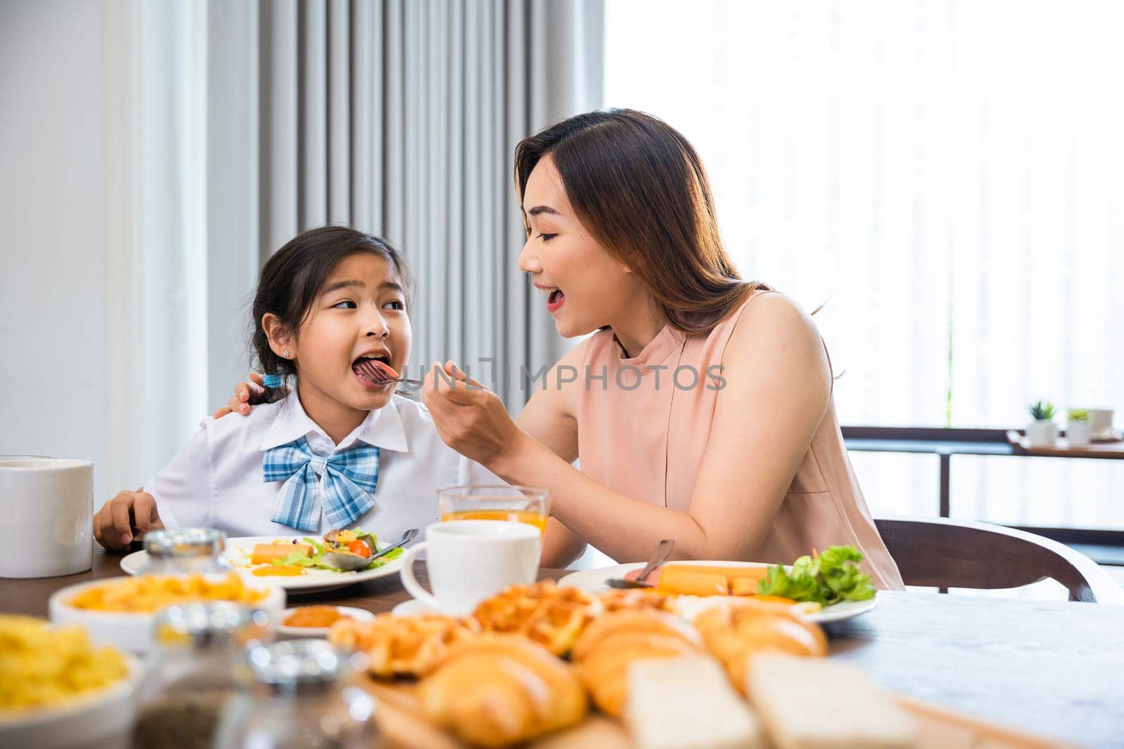 Family breakfast. Mom and little preschooler have fun smile eating meal together, Asian mother and child daughter having breakfast on food table, Healthy food at home in morning before go to school