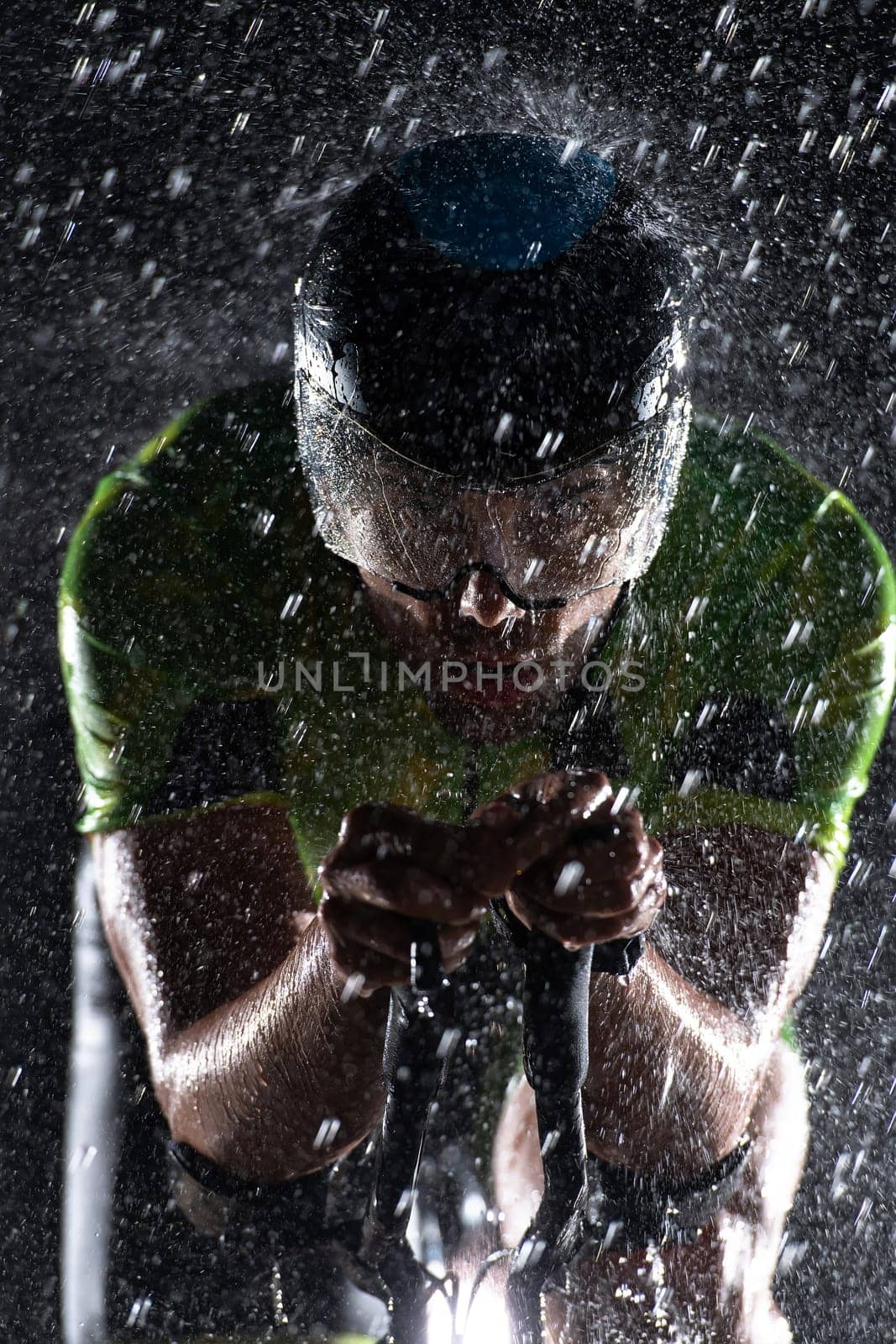 A triathlete braving the rain as he cycles through the night, preparing himself for the upcoming marathon. The blurred raindrops in the foreground and the dark, moody atmosphere in the background add to the sense of determination and grit shown by the athlete