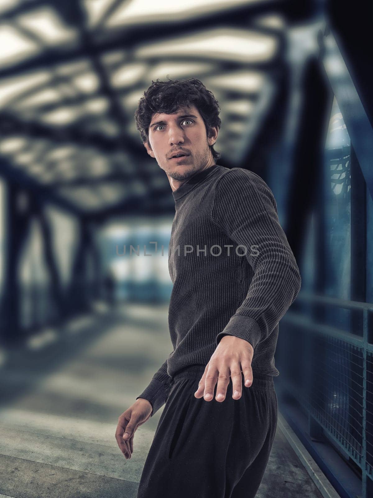 A young man standing on a bridge, running away looking scared or worried, ready to flee