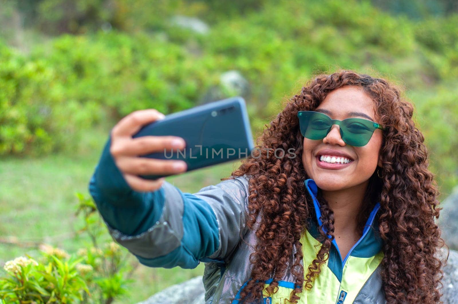 pretty latina and tourism vlogger with green glasses and curly hair showing her followers the mountain place where she is. High quality photo
