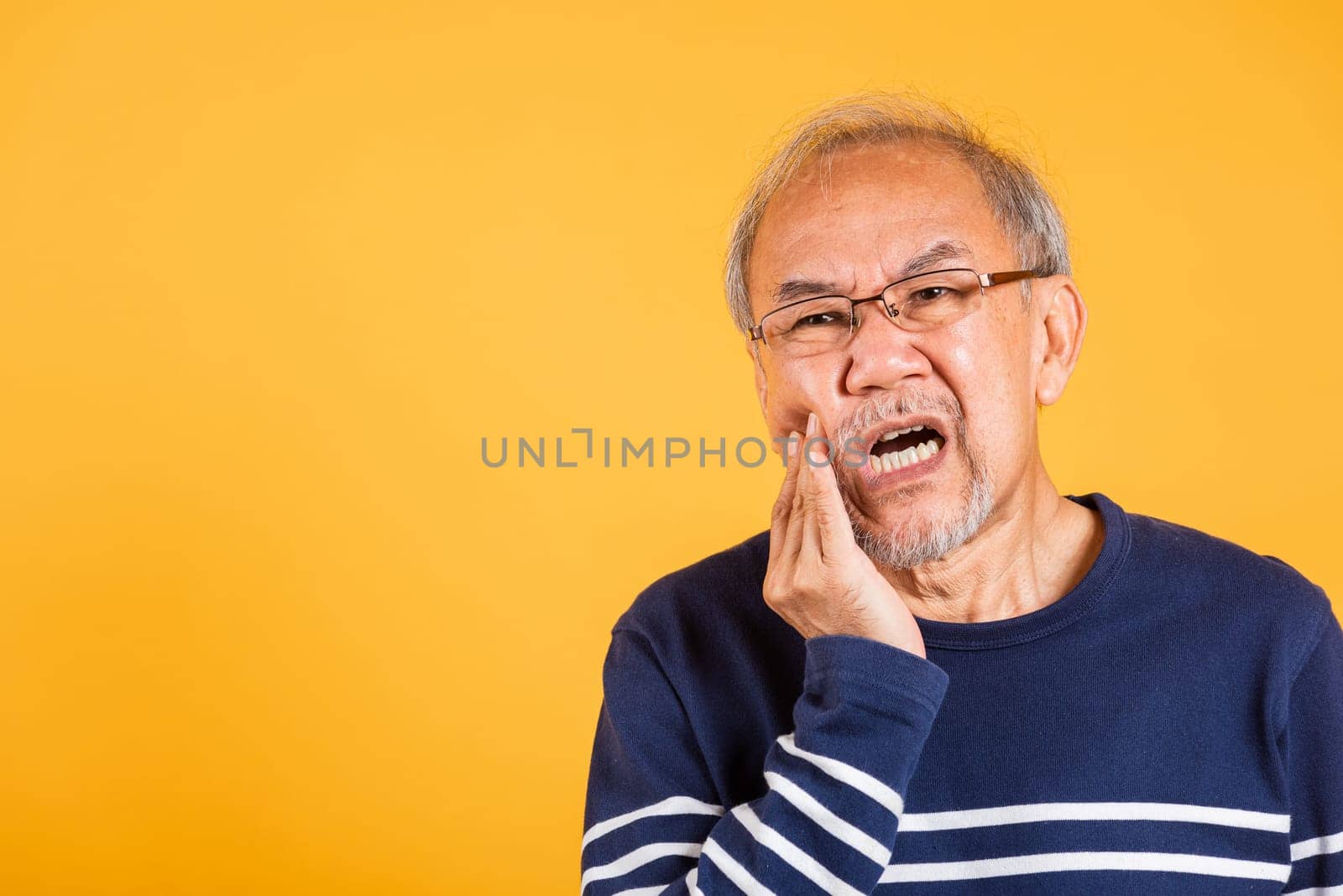 Dental pain. Portrait senior old man sad hand touching cheek suffering from toothache studio shot isolated on yellow background, Asian unhappy elder man problems with teeth pain, dental healthcare