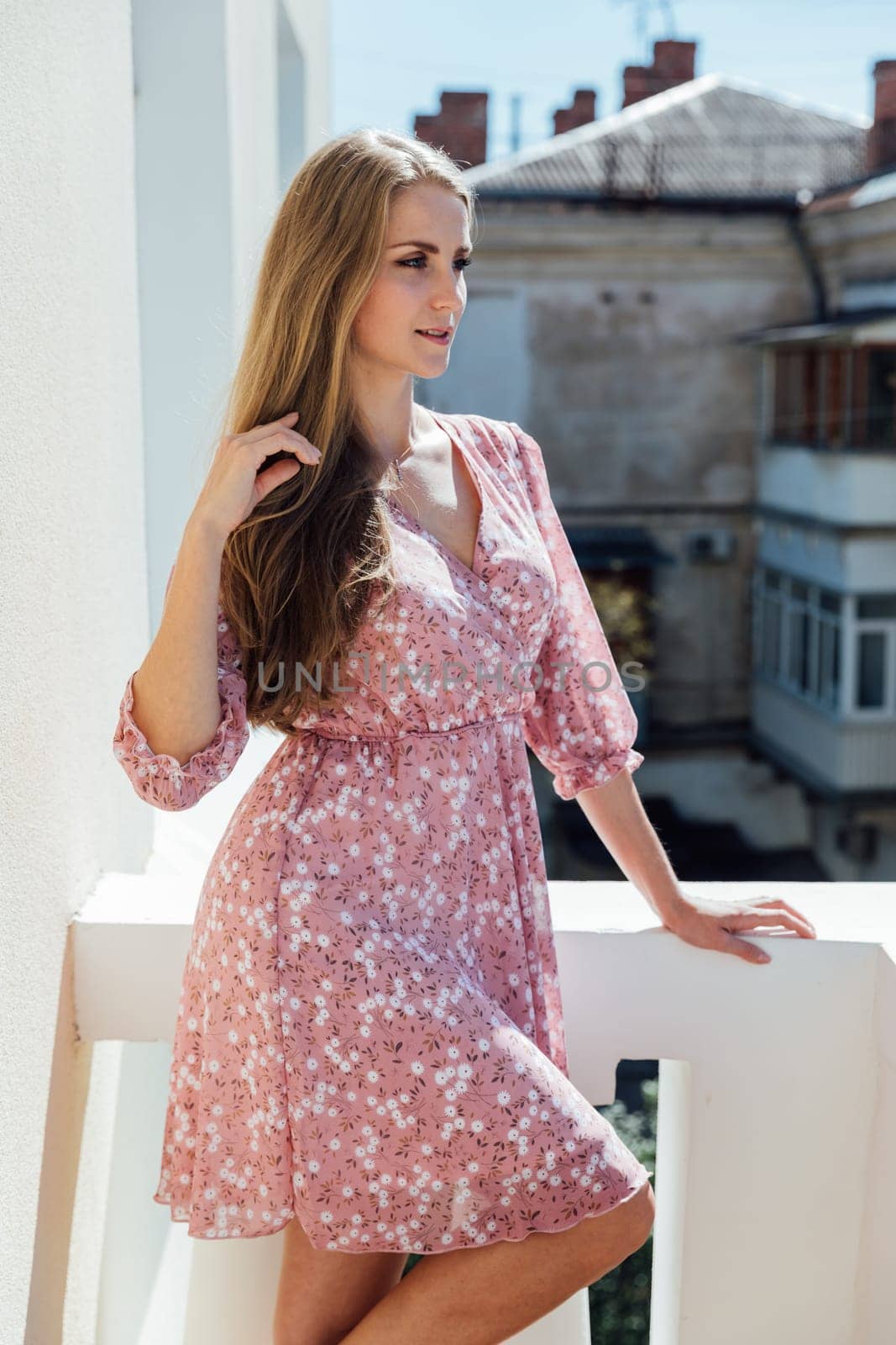 Beautiful blonde woman in pink dress posing on the balcony of the room