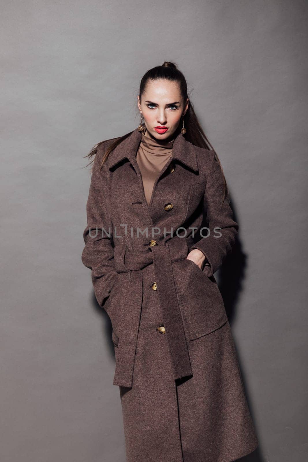 Beautiful fashionable woman in a raincoat on a gray background by Simakov