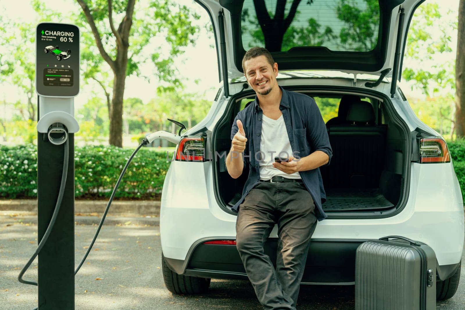Man using smartphone online banking application to pay for electric car battery charging from EV charging station during vacation holiday road trip at national park or summer forest. Exalt