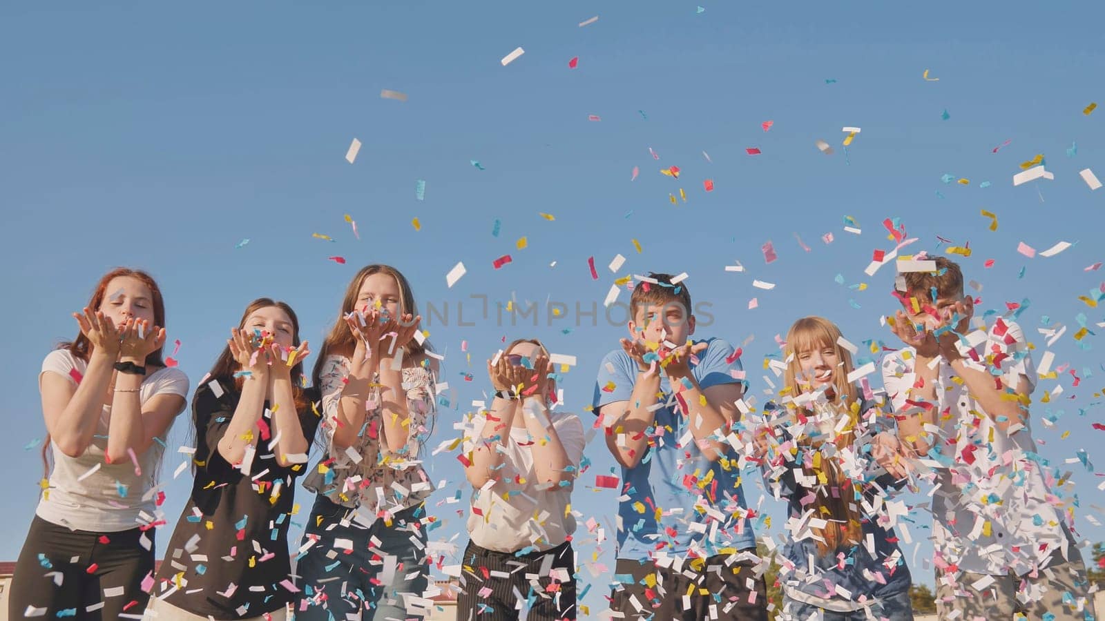 Friends blow colorful paper confetti on a sunny day