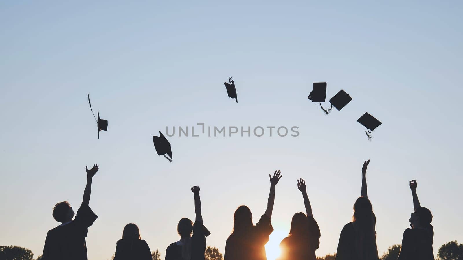 Silhouettes of Happy college graduates tossing their caps up at sunset