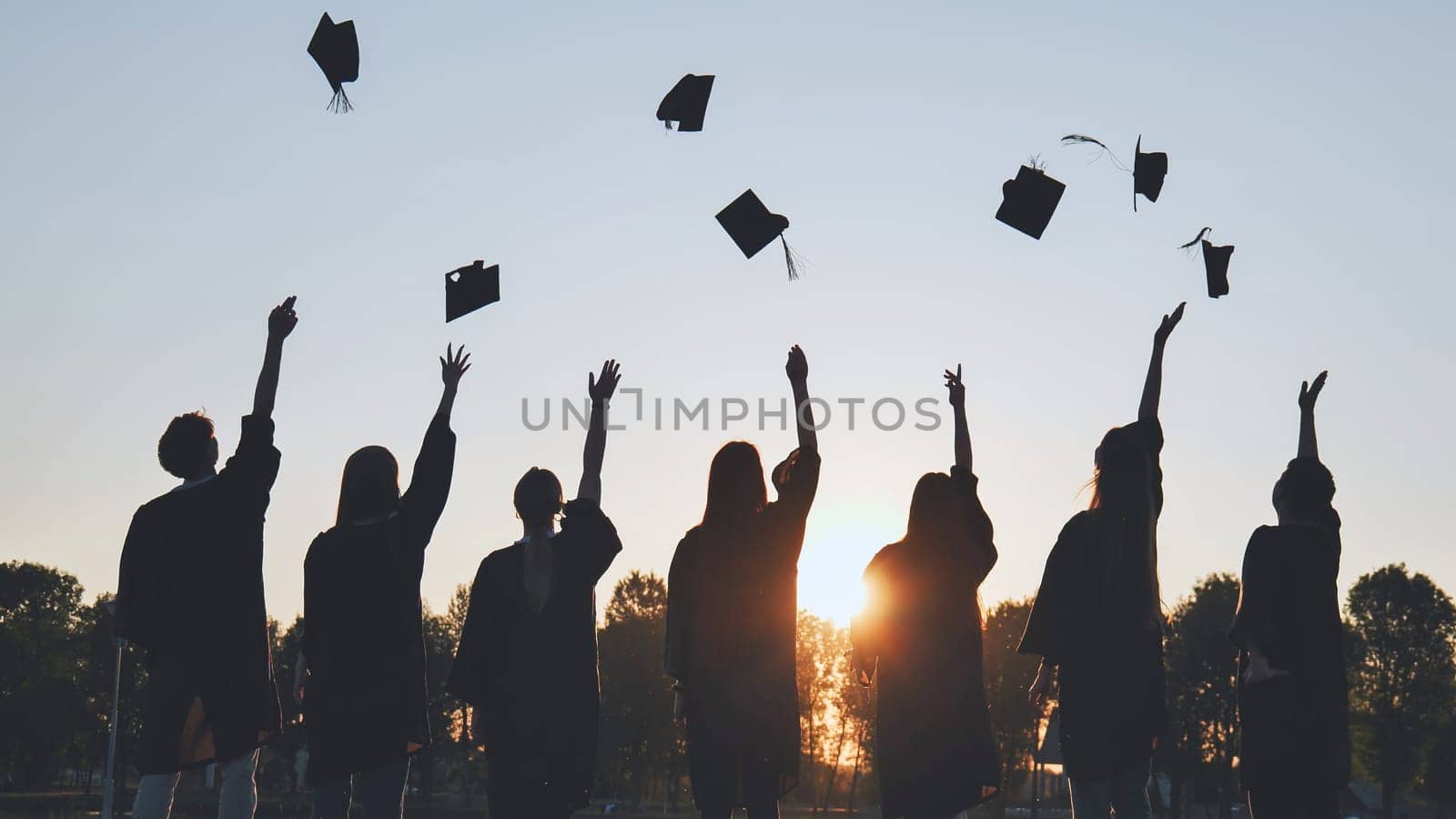 Silhouettes of Happy college graduates tossing their caps up at sunset