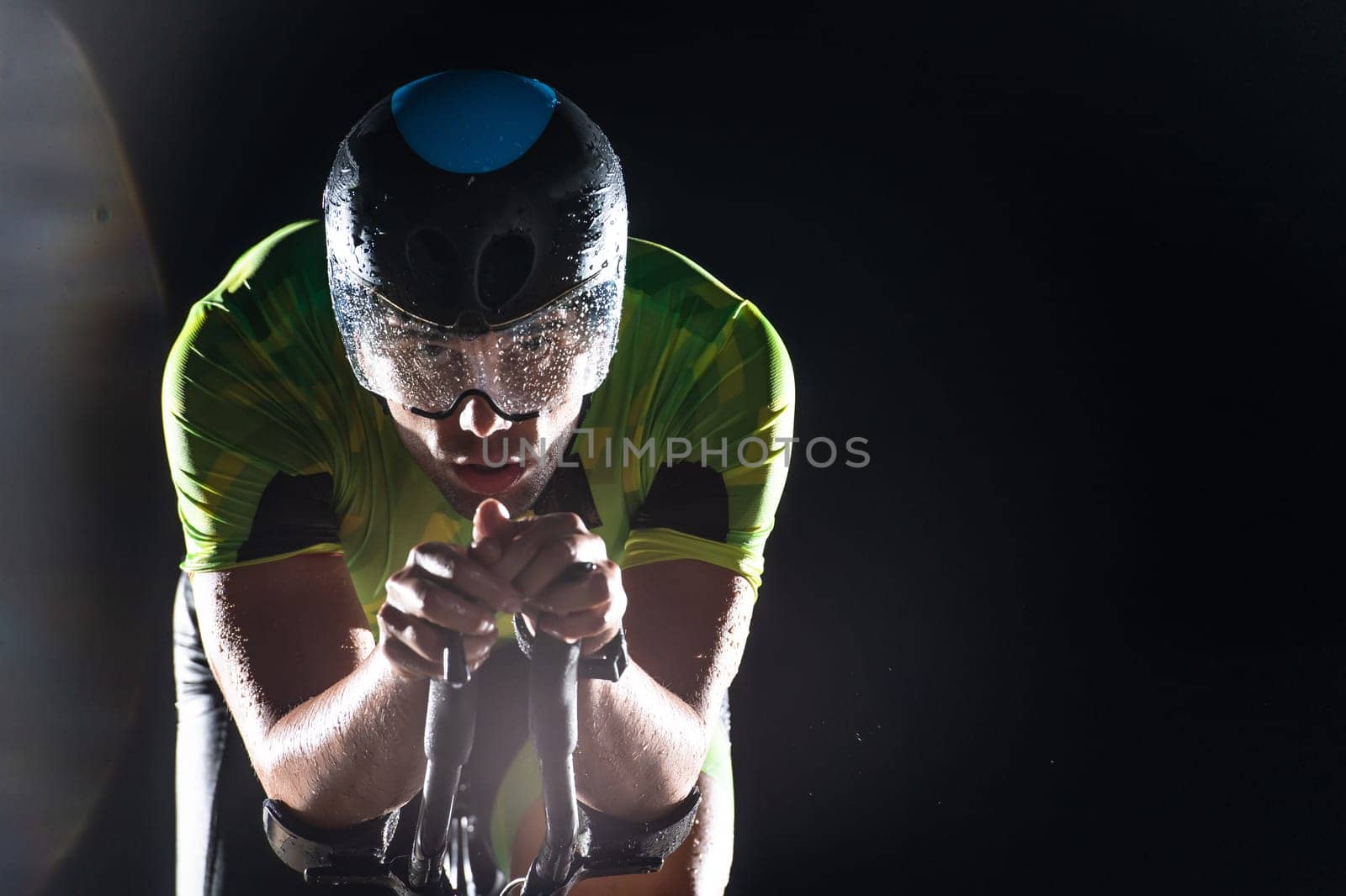 A triathlete rides his bike in the darkness of night, pushing himself to prepare for a marathon. The contrast between the darkness and the light of his bike creates a sense of drama and highlights the athlete's determination and perseverance
