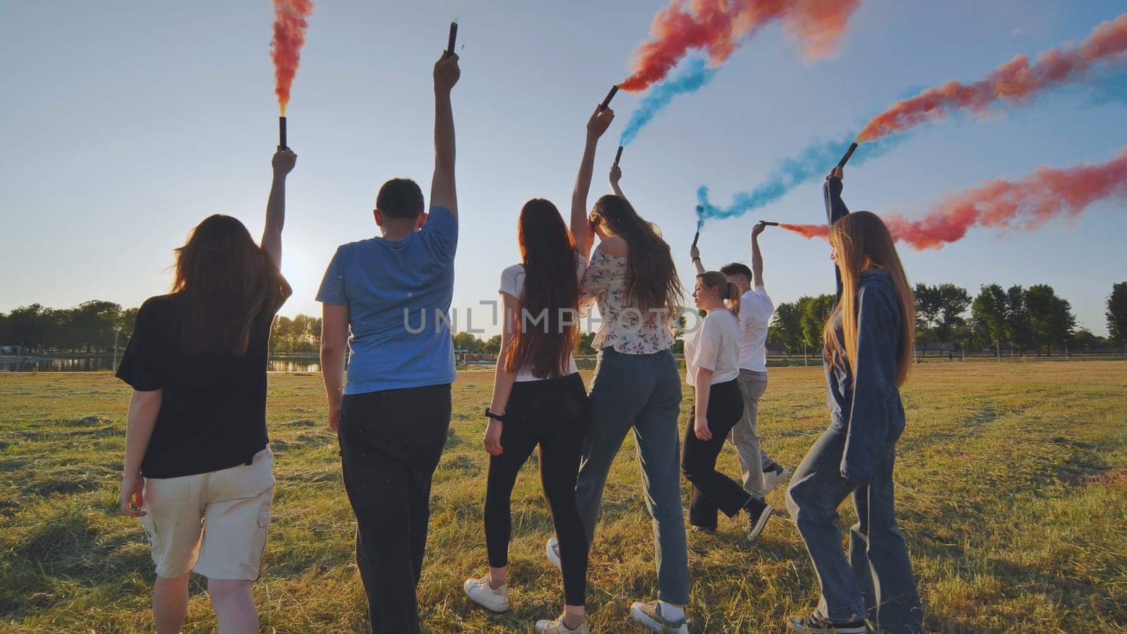 A group of friends spraying multi-colored smoke at sunset. by DovidPro