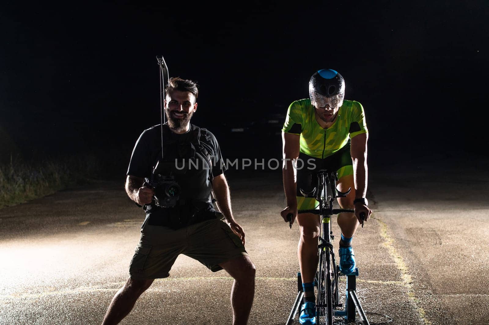 Behind the scenes. Professional videographer on a night shoot with a triathlete riding a bicycle for video recording purposes by dotshock