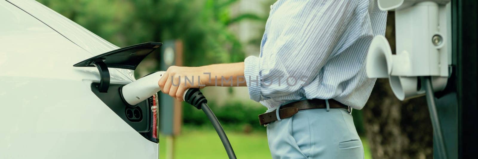 Young woman recharging battery for electric car during road trip. Exalt by biancoblue