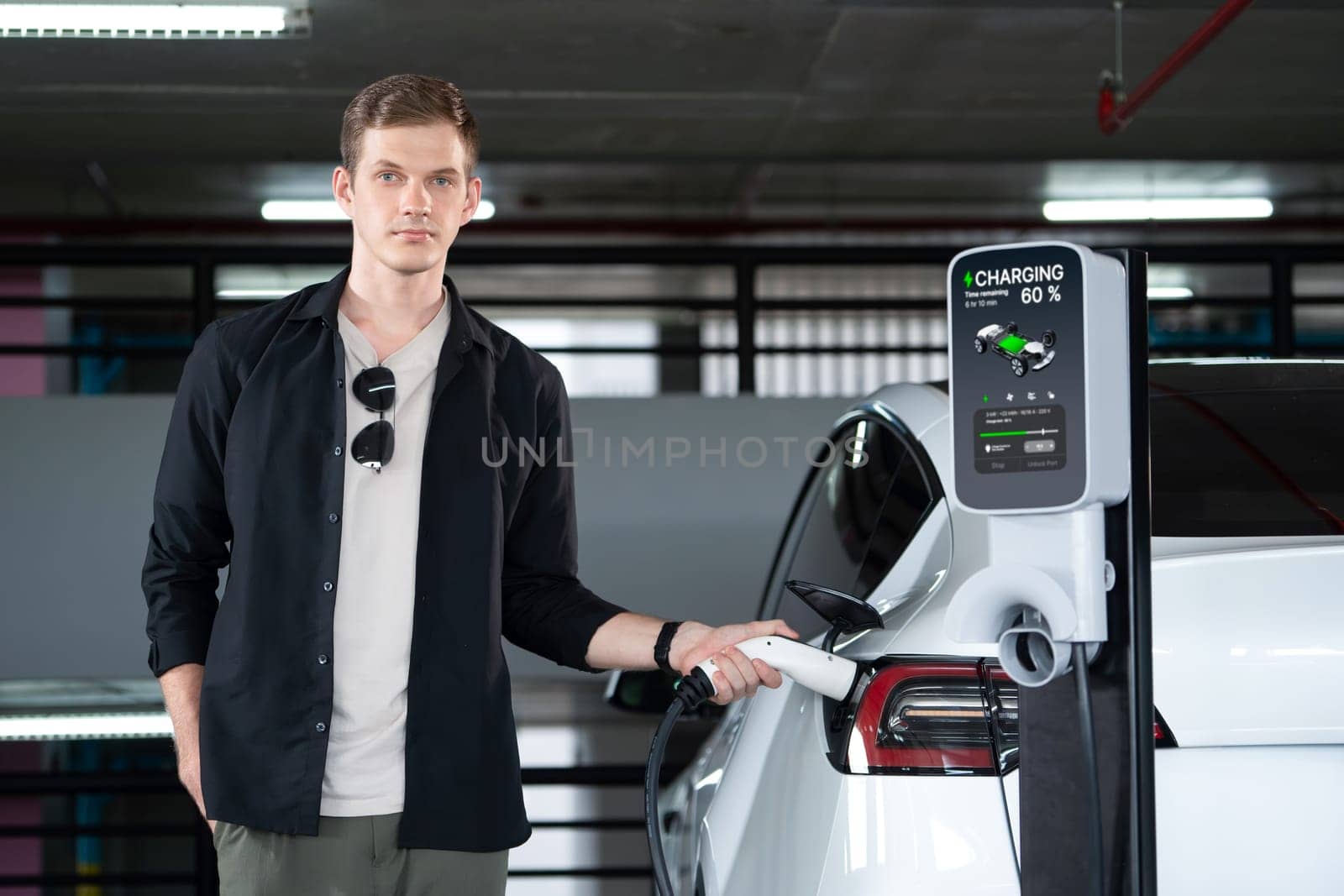 Young man travel with EV electric car to shopping center parking lot charging in downtown city showing urban sustainability lifestyle by green clean rechargeable energy of electric vehicle innards