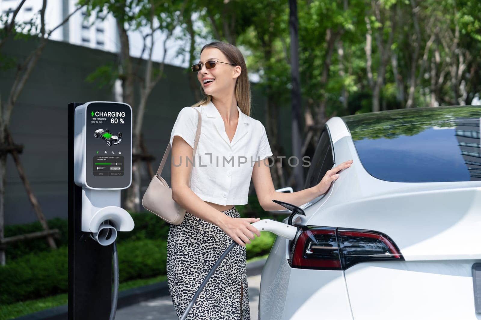 Young woman travel with EV electric car charging in green sustainable city outdoor garden in summer. Urban sustainability lifestyle by green clean rechargeable energy of electric BEV vehicle innards