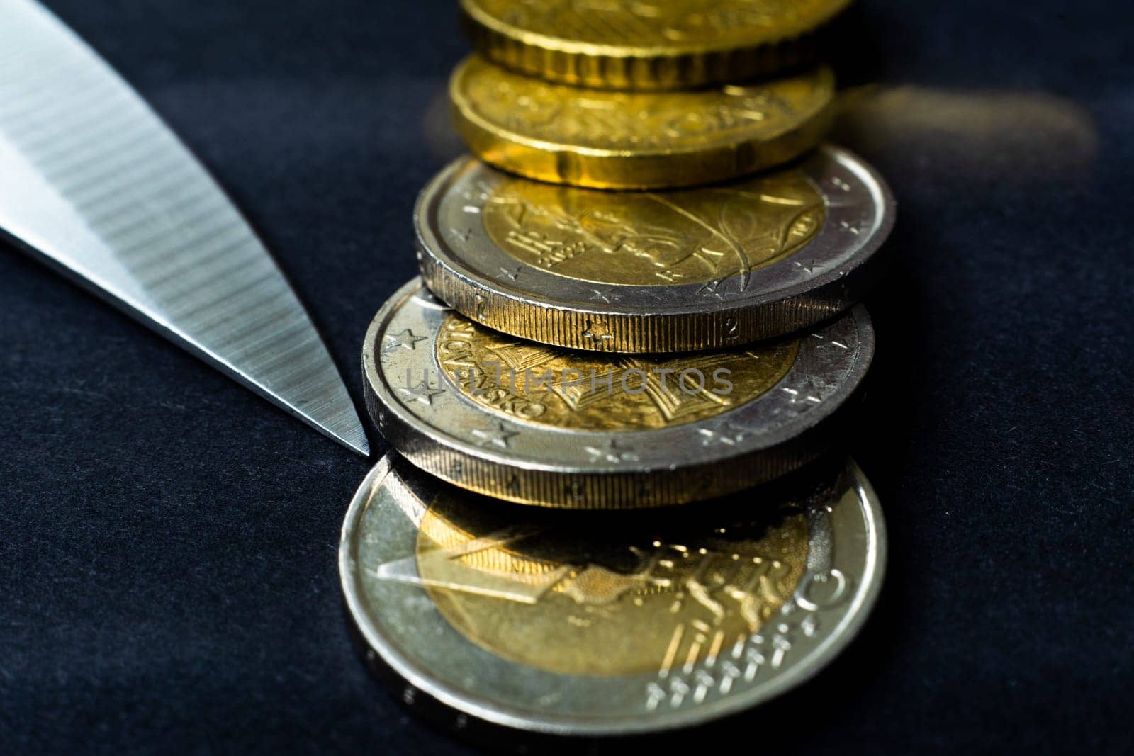 Money concept. Knife with coins euro, close up, dark black background