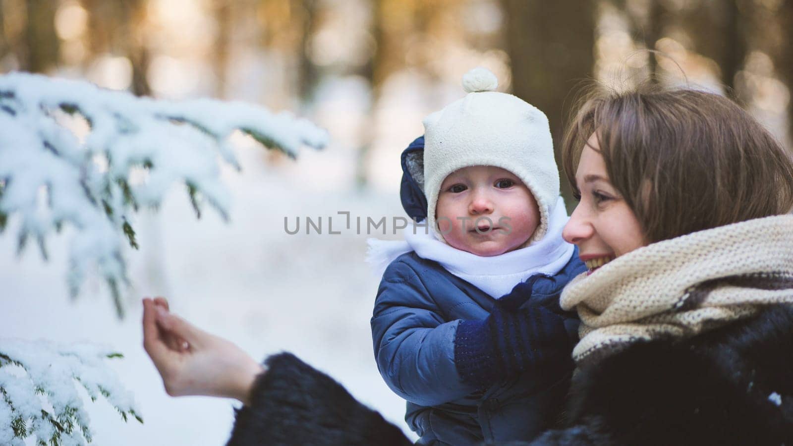 A mother shows her child a branch in a snow-covered forest