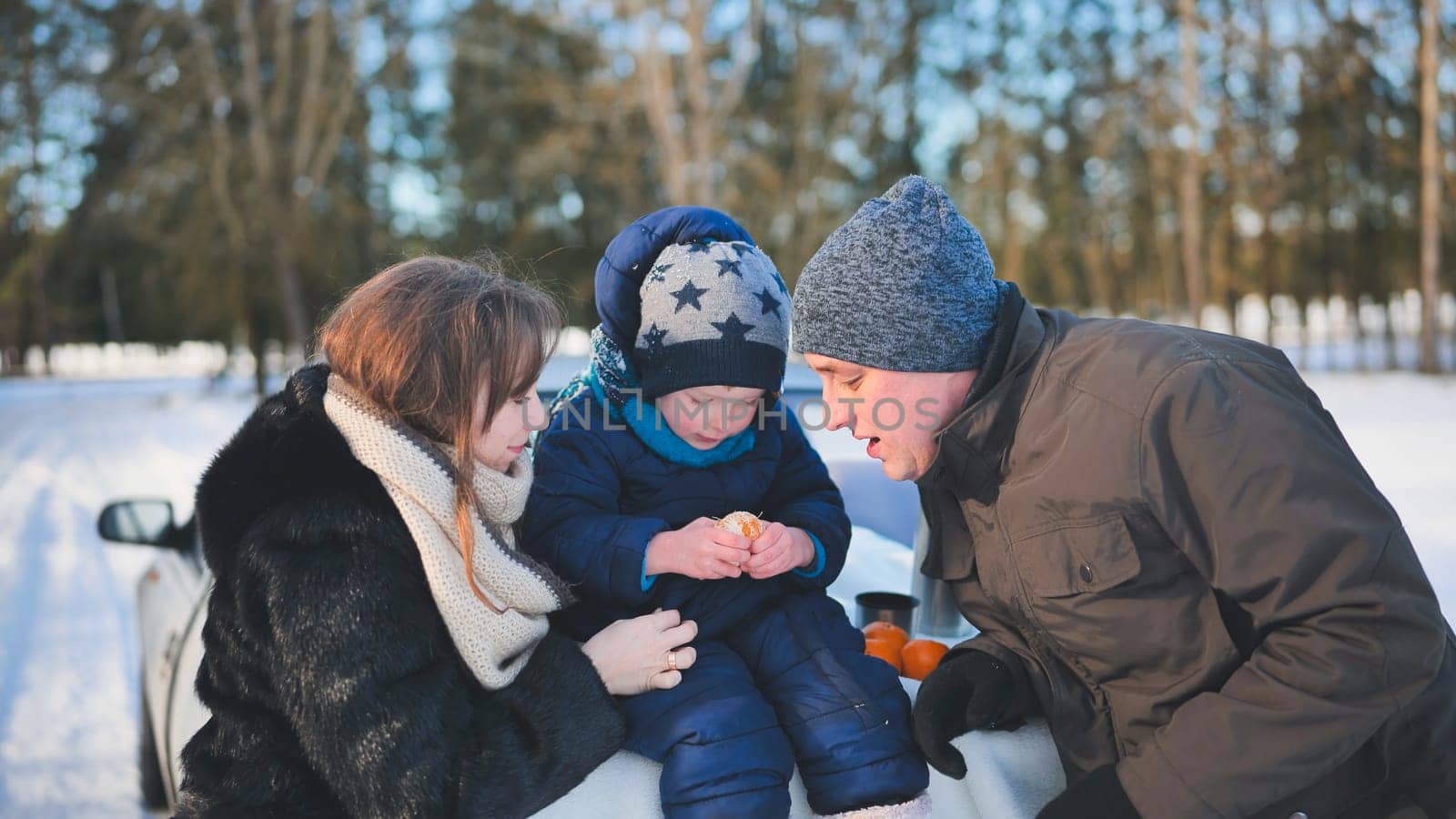 A young family is eating tangerines during a picnic on a winter day