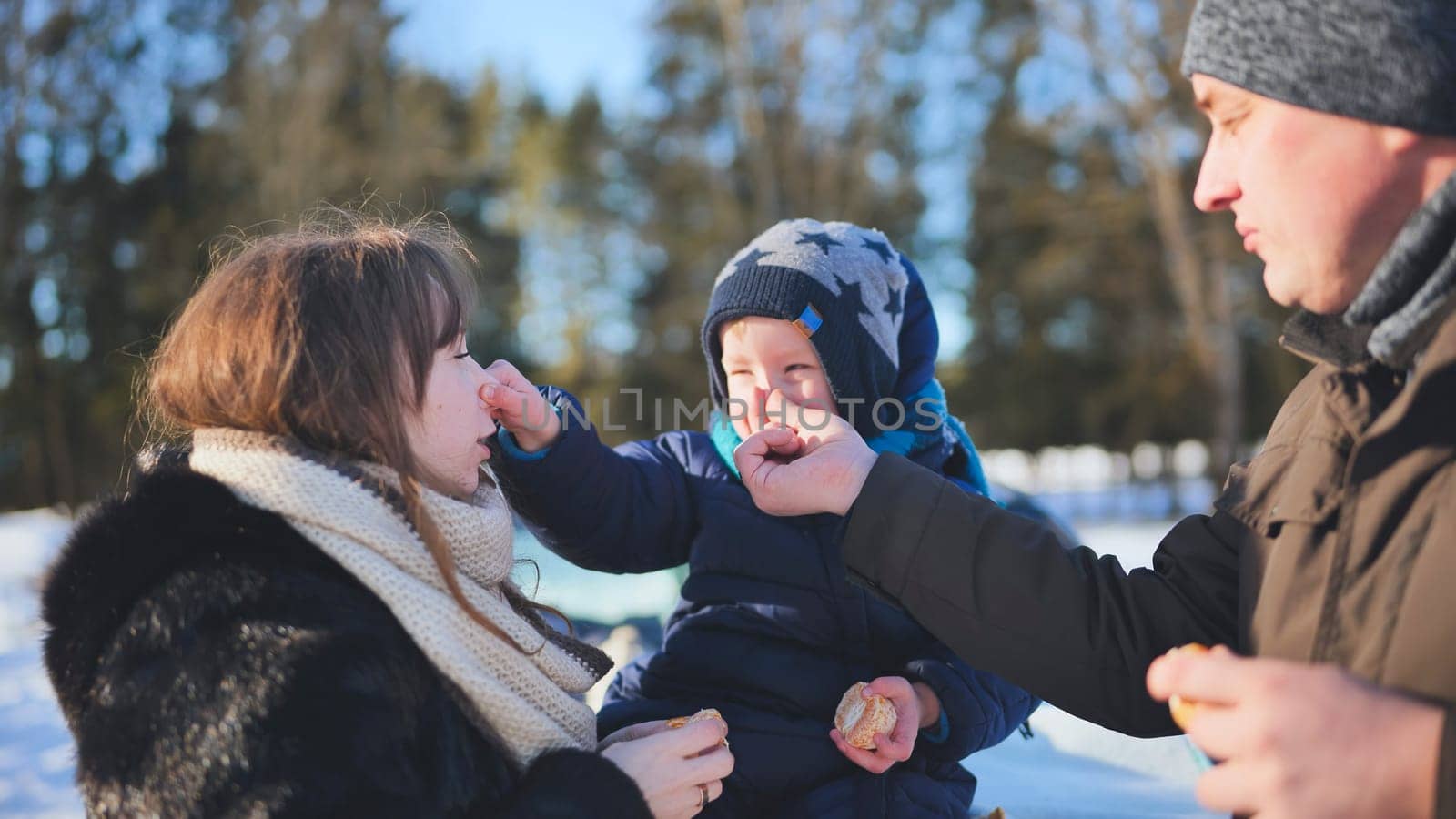 A young family is eating tangerines during a picnic on a winter day. by DovidPro