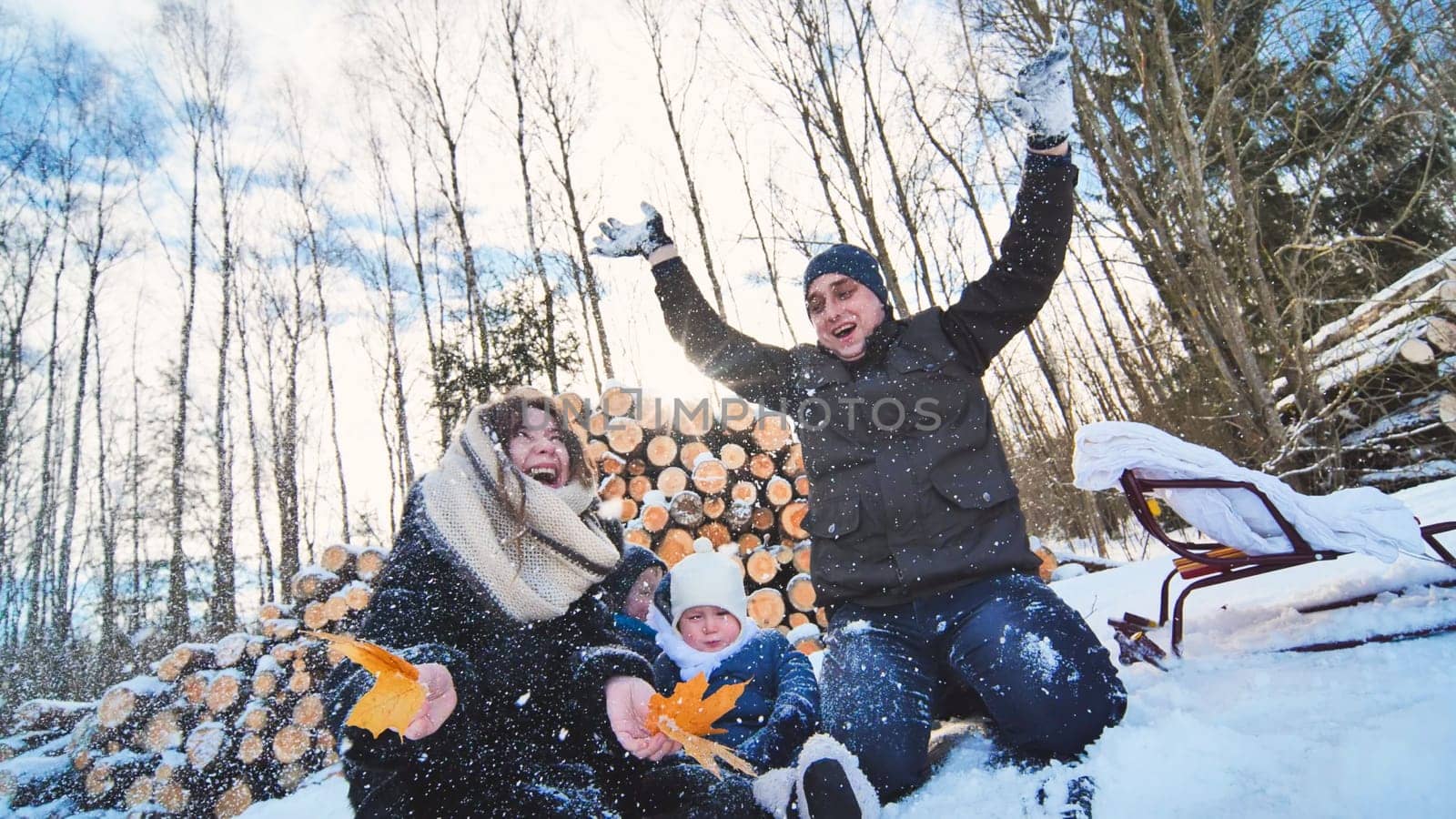 Concept of the transition from fall to winter with the help of an autumn leaf. A happy family in the woods in winter. Father tossing snow