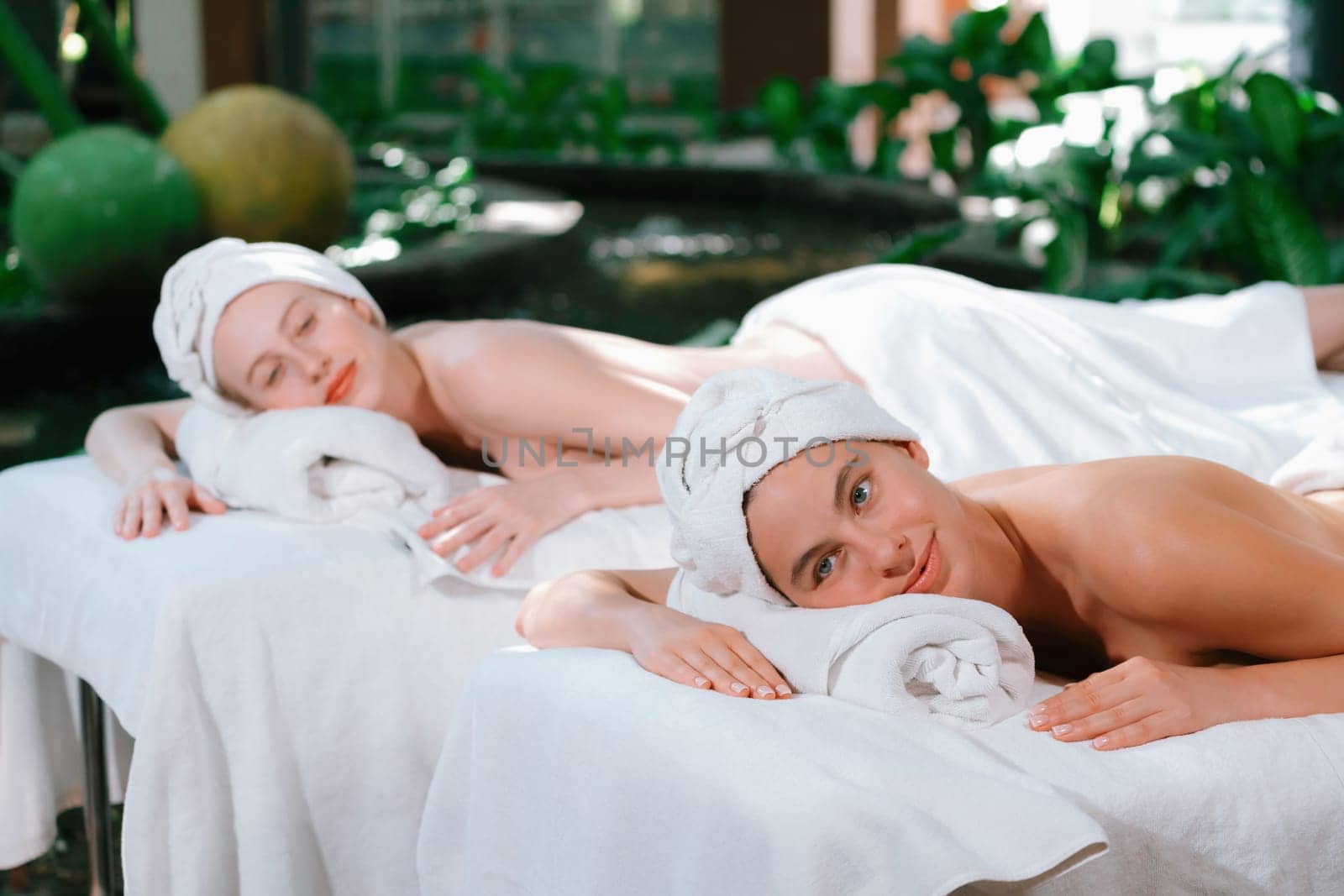 A portrait of a couple of a beautiful young caucasian woman with white towel rest on comfortable spa bed with relaxation while having body massage with professional masseur at spa salon.Tranquility.