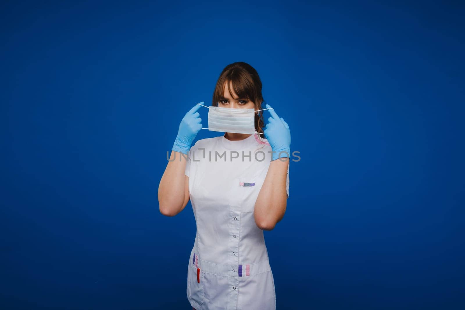 A doctor girl stands in a medical mask on an isolated blue background