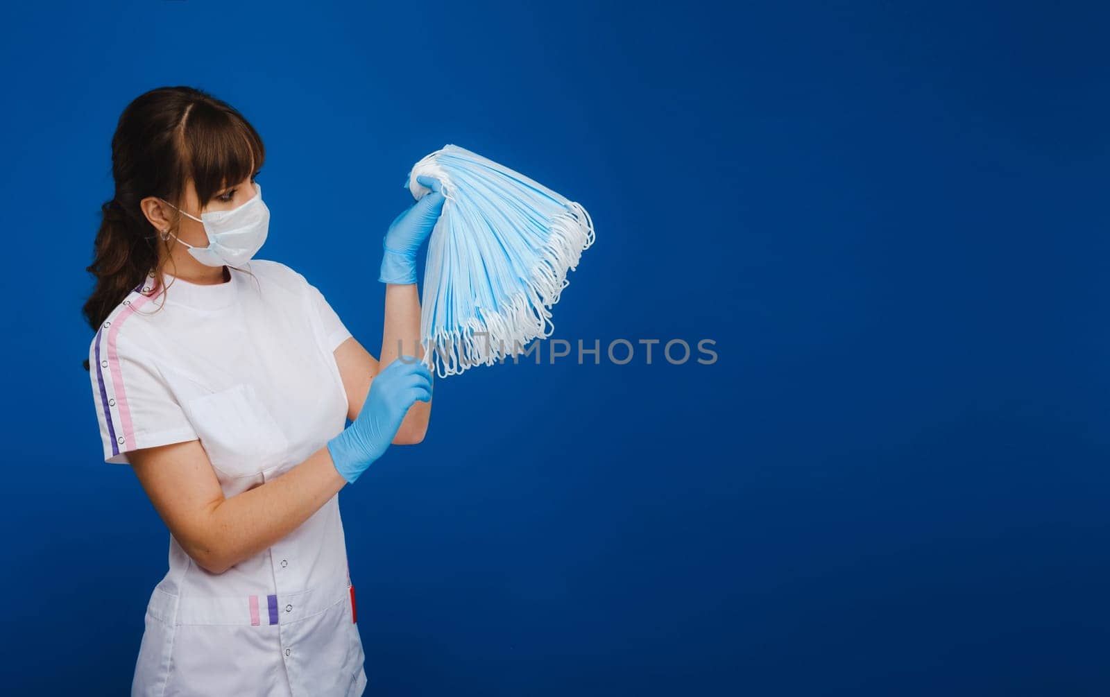 a doctor girl in a medical mask on a blue background holds a lot of protective masks in her hands.