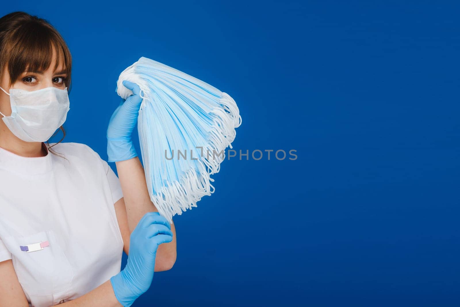 A young girl doctor in a medical mask holds a lot of masks in her hands. A nurse poses on a blue background.