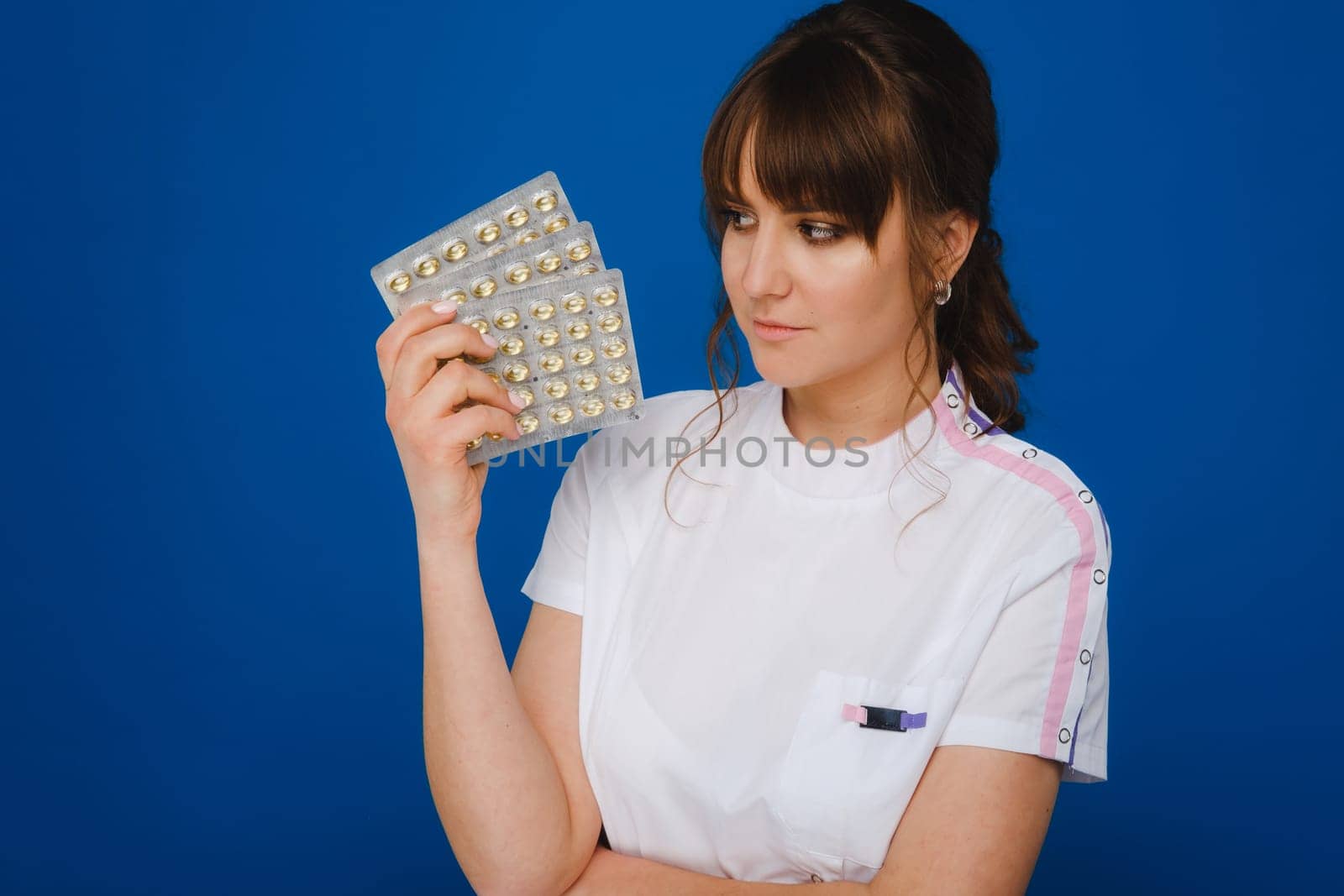 The concept of health care. A young brunette doctor in a white coat on a blue background shows plates with capsules to take