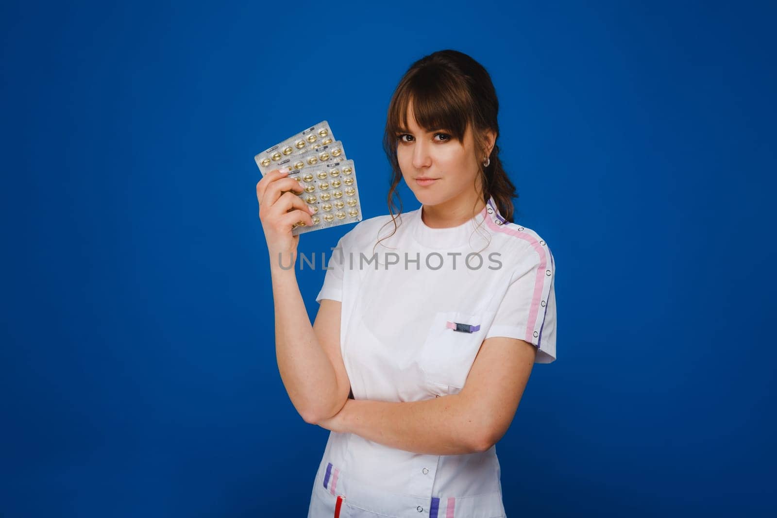 The concept of health care. A young brunette doctor in a white coat on a blue background shows plates with capsules to take