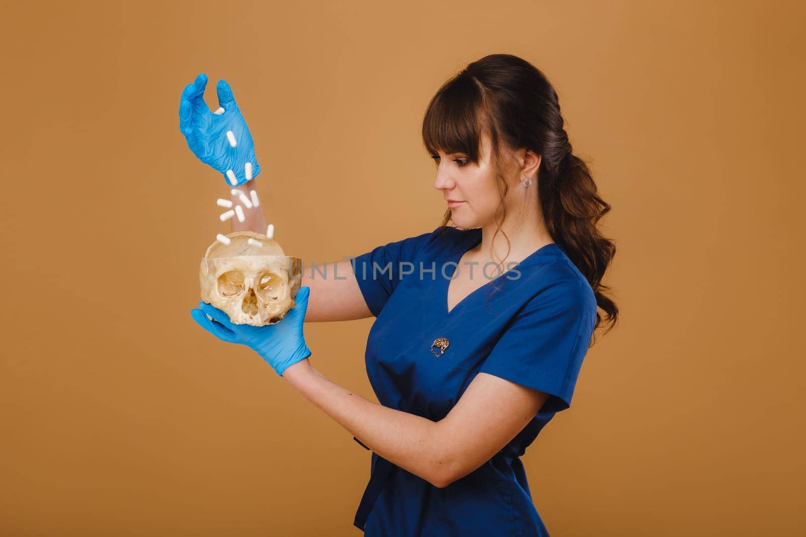 Cute young doctor girl holding a human skull, brown background behind the doctor.