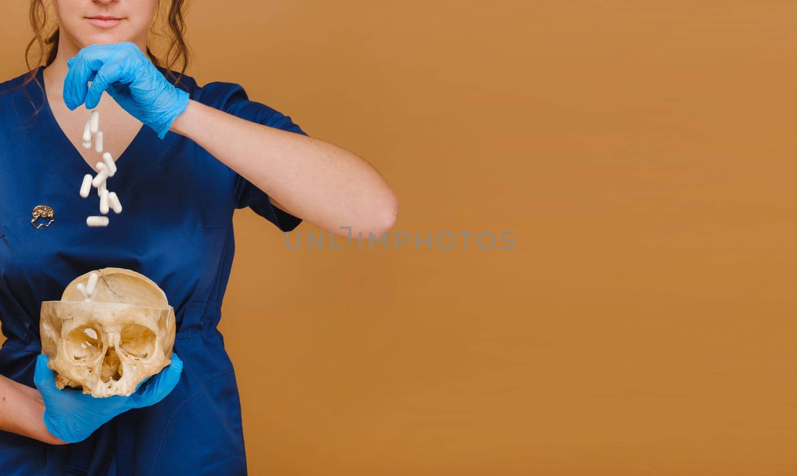 A pretty young doctor pours vitamin capsules into a human skull. The doctor pours pills on the background