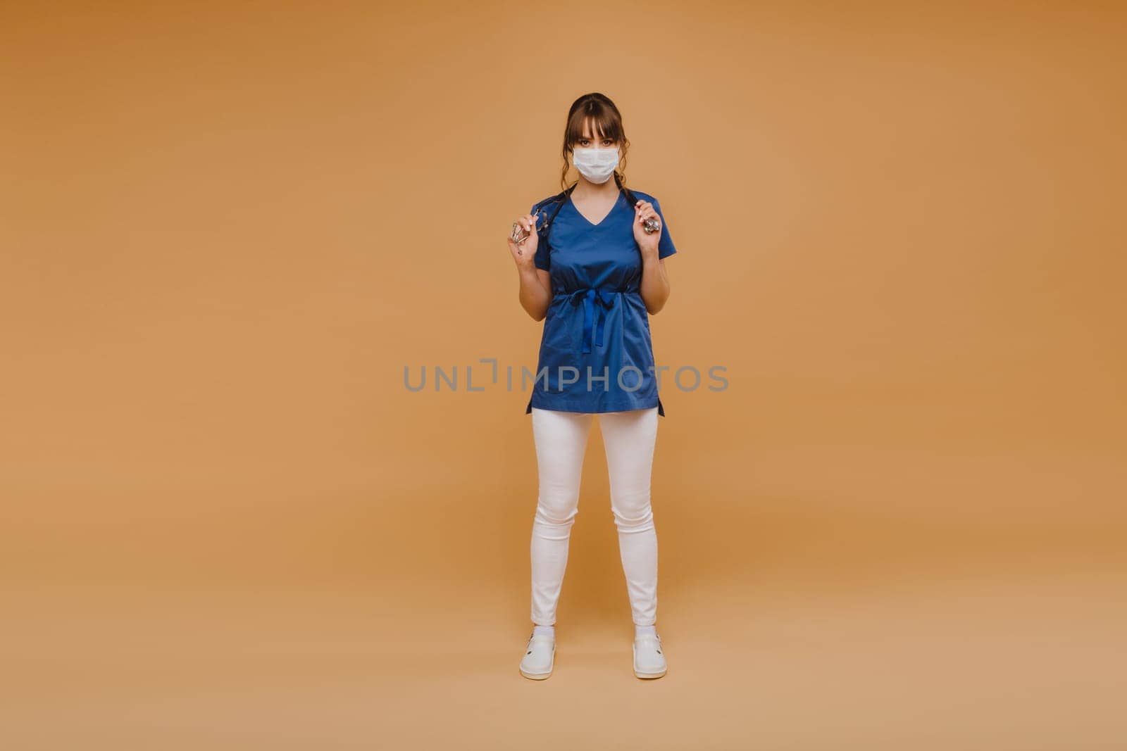 A girl doctor stands in a medical mask, isolated on a gray background