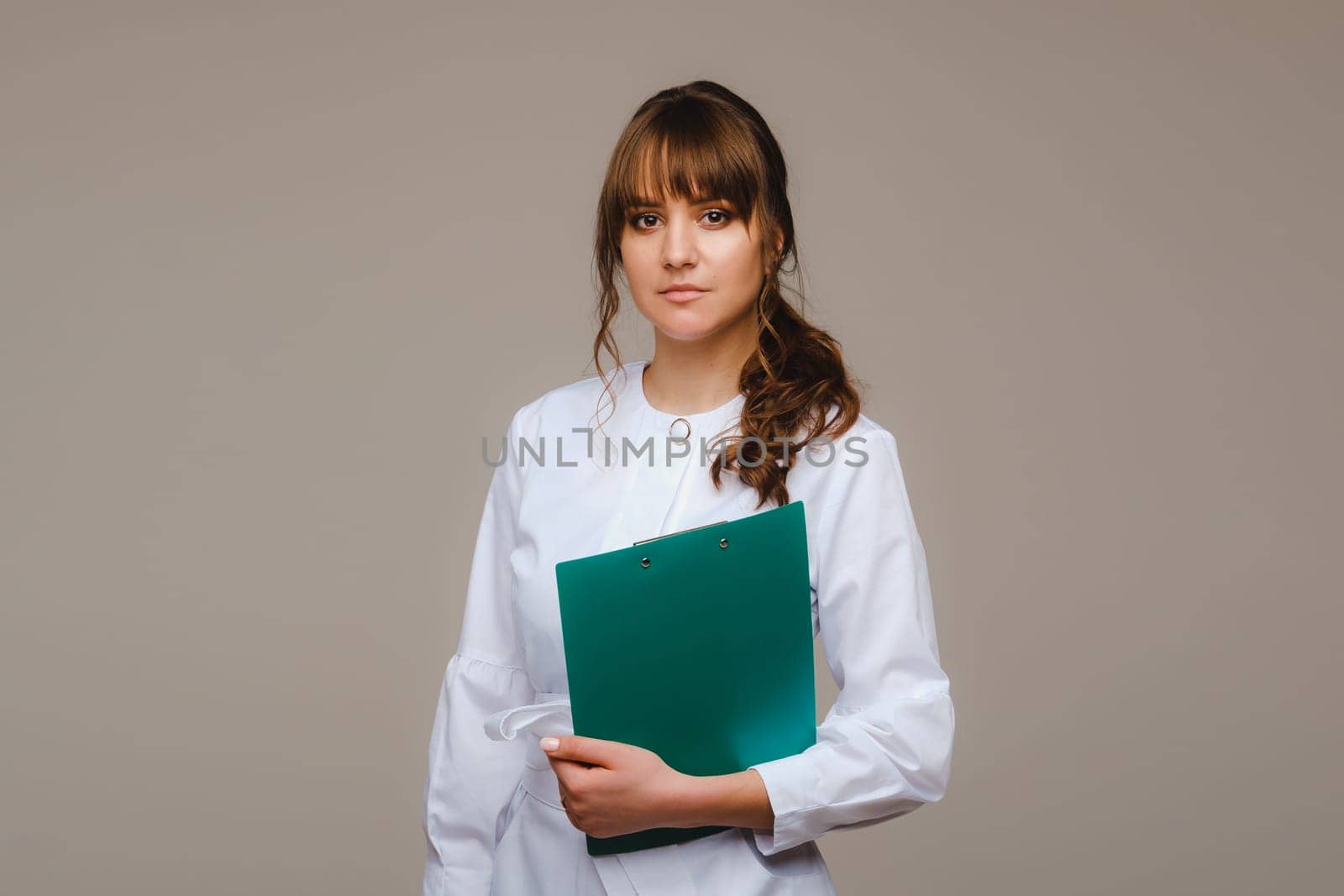 Portrait of a female medical worker in a gray background with a medical report.Girl doctor with a Notepad by Lobachad