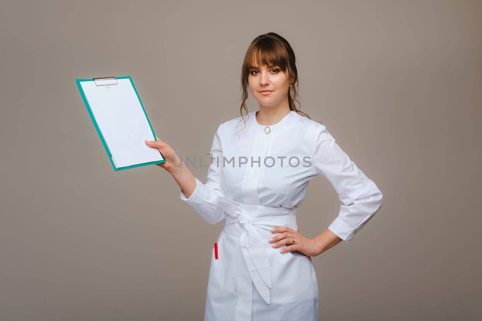 Portrait of a female medical worker in a gray background with a medical report.Girl doctor with a Notepad by Lobachad