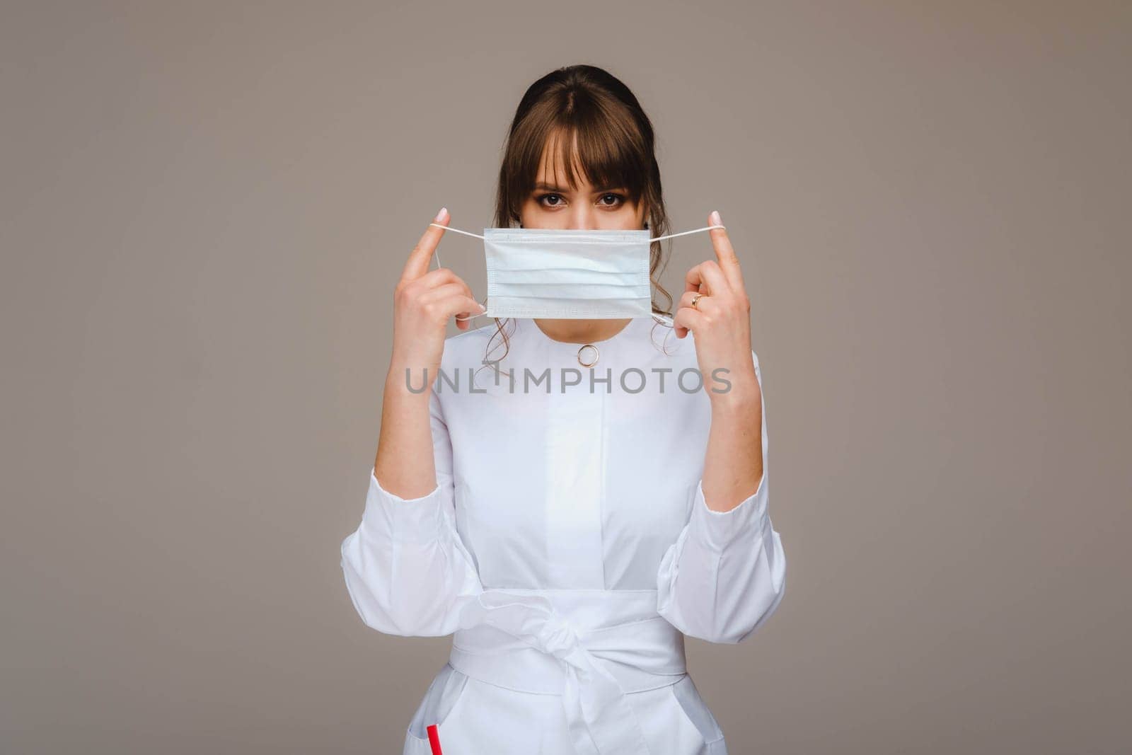 A girl doctor stands in a medical mask, isolated on a gray background