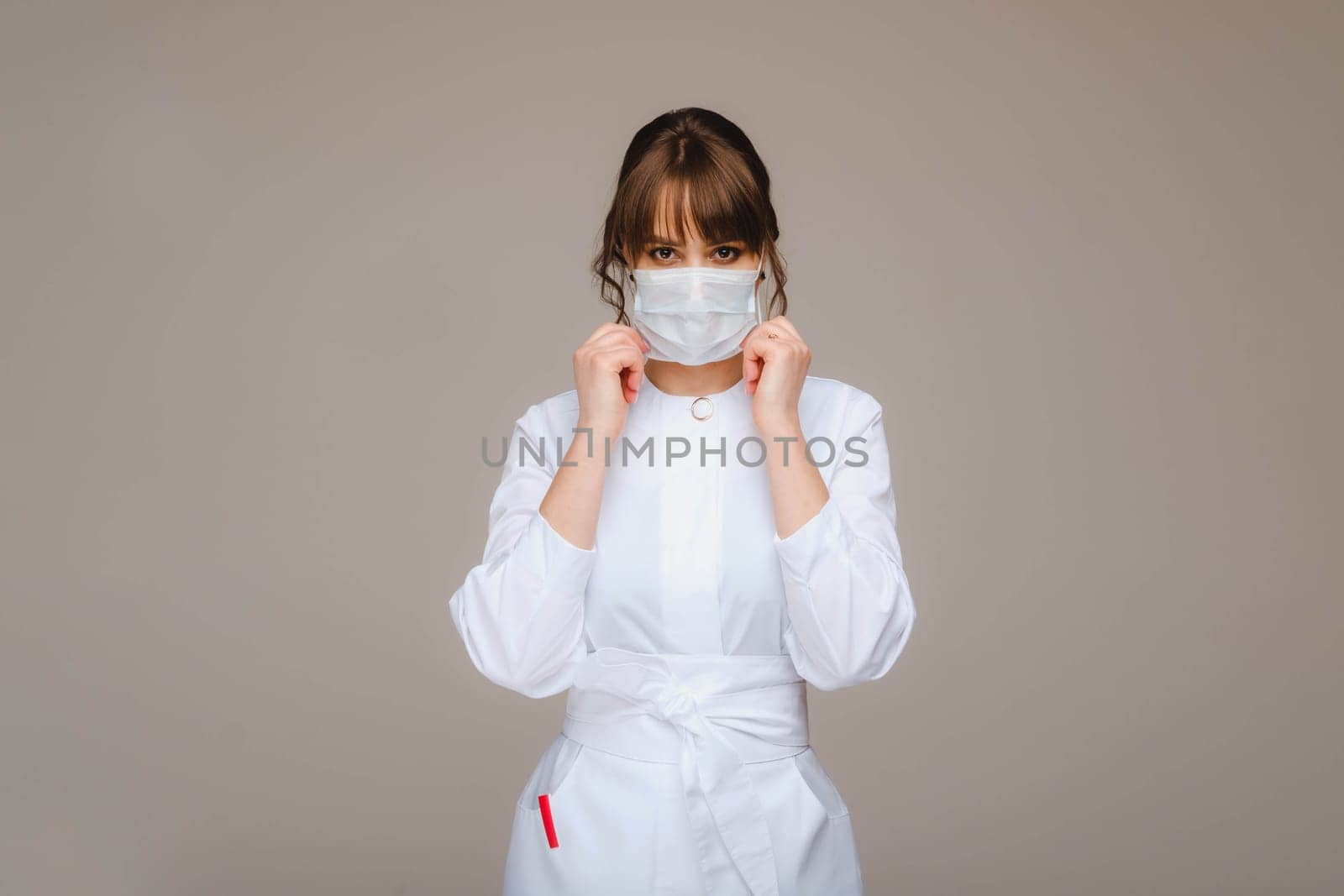 A girl doctor stands in a medical mask, isolated on a gray background. by Lobachad