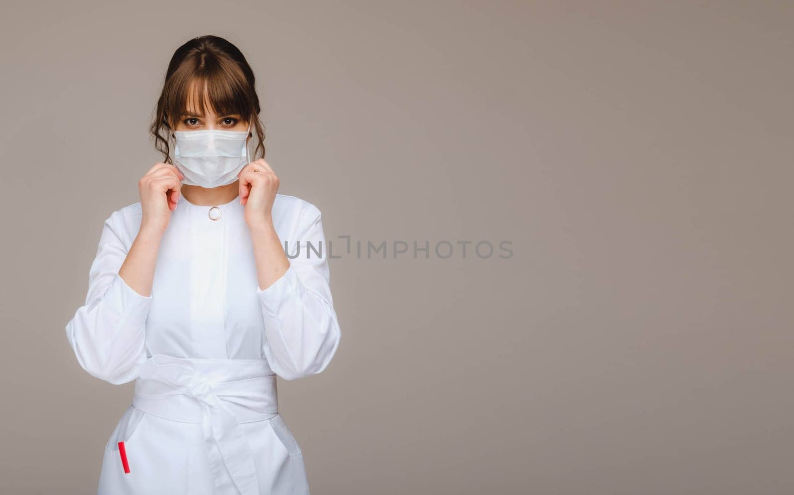 A girl doctor stands in a medical mask on a gray background by Lobachad