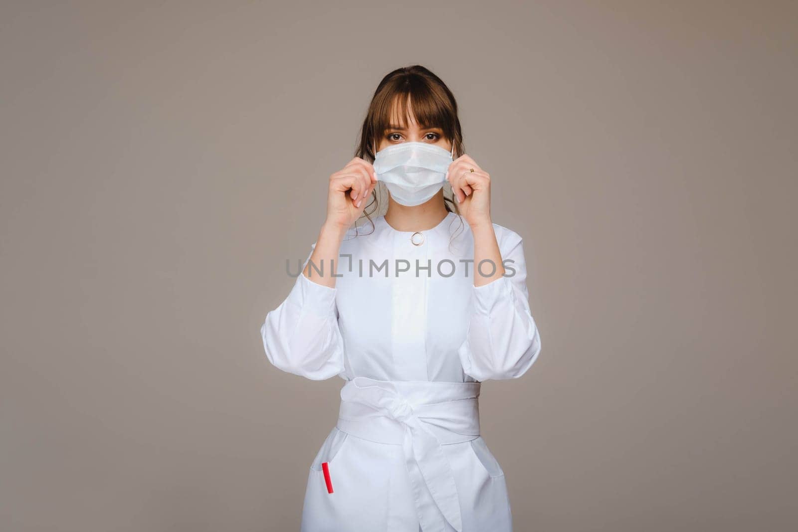 A girl doctor stands in a medical mask, isolated on a gray background. by Lobachad